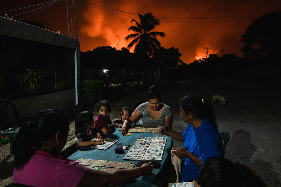 PUNTA DE MATA, VENEZUELA - NOVEMBER 5, 2022: Neighbors play board games under a sky lit by gas flares. Adriana Loureiro Fernandez for The New York Times